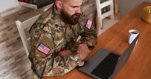 American soldier man in military uniform using computer laptop at home