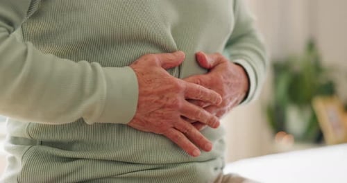 Hands, stomach and senior person with pain in home for disease, tummy cramps and digestive problem