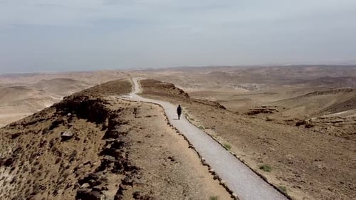 aerial backward slow drone shot of a single person walking on a mountain trail in the middle of an e
