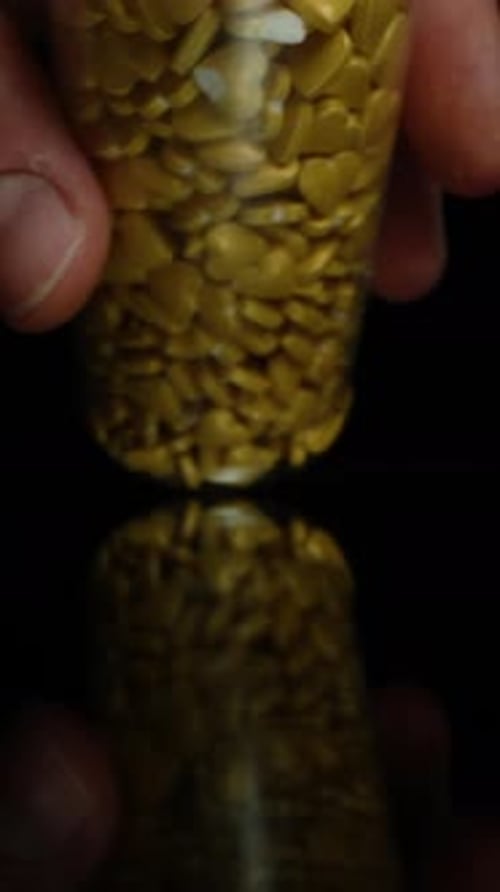 Vertical. Golden Hearts Pour onto the Table, the Camera Moves Backwards, Capturing Macro Shots