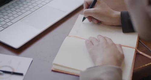 Closeup of Female Hand Writing in Notebook While Businesswoman Working at Table in Office