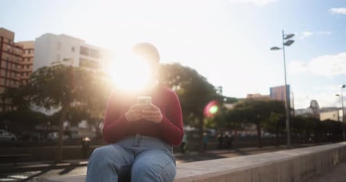 Woman Using Phone While Sitting on Ledge in City
