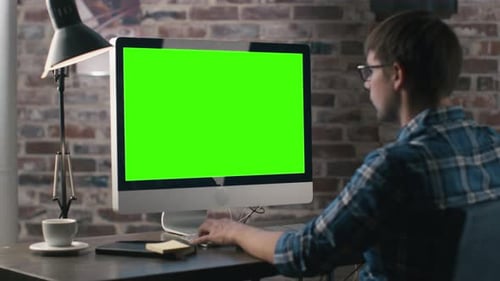 Young man is working on a computer with a mock-up green screen.