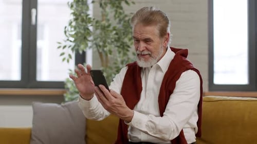Senior Man Using Smartphone on Gold Couch Indoors