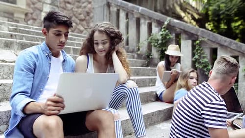 Teenage students on stone steps with gadgets at sunny university campus