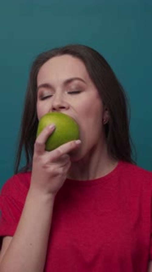 Une femme tenant une pomme verte fraîche dans un studio lumineux dégageant des vibrations joyeuses
