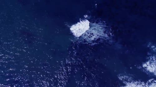 Blue ocean water with rocks visible below, top down drone shot