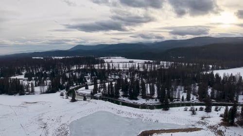 Aerial drone footage of a snow-covered landscape with a winding frozen lake and surrounding