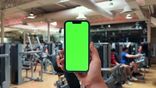 Girl Hand Holding a Smartphone with Empty Green Screen Chromakey at the Gym