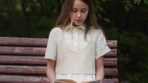 Teenage Girl Reading Book While Sitting on Bench at Park