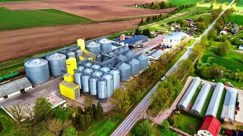 Aerial drone view of grain silos, farmland and greenhouses in springtime rural setting