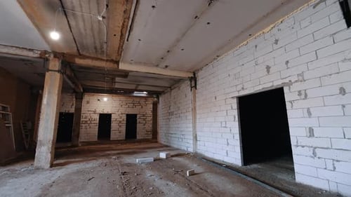 Walking inside the spacious room of a building with shabby ceiling and white brick walls.