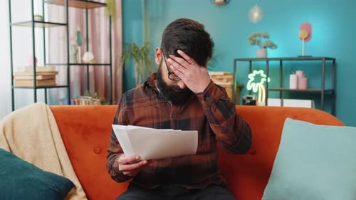 Frustrated Upset Angry Businessman Works with Paperwork Reports Documents on Laptop at Home Couch