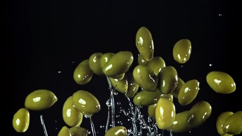 Green Olives Falling with Water on Black Background