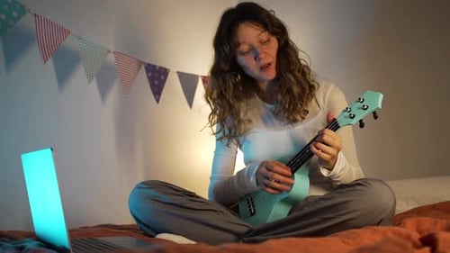 Woman Plays Ukulele and Sings on Bed
