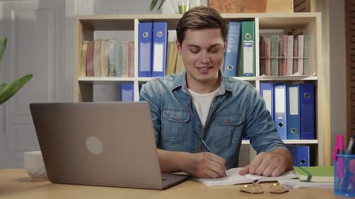 Joven atractivo e inteligente que trabaja como gerente de oficina contactando a los clientes en línea tomando notas usando