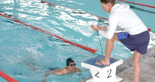 A Caucasian coach is timing a swimmer's lap