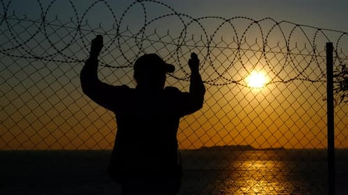 Refugee Silhouette Standing Behind Barbed Wire Fence