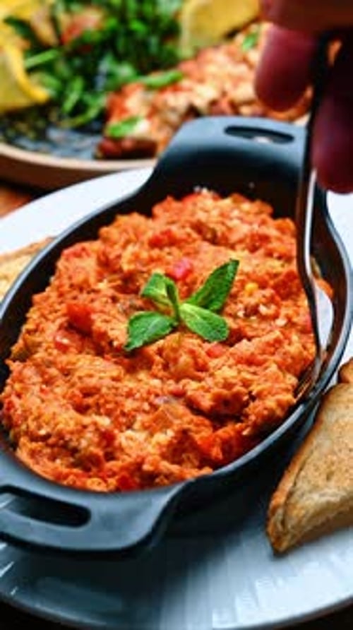 Persona que muerde shakshuka con un tenedor plateado. Primer plano de un tomate levantando una horquilla