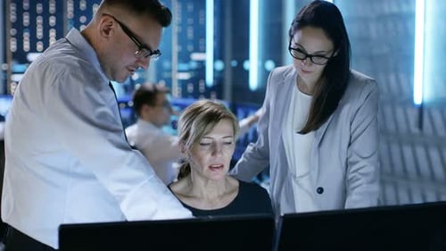 Ein Team von Systemanalysten diskutiert über den Monitoring-Raum. Im Hintergrund Leute, die mit M arbeiten