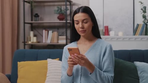 Young Woman Using Mobile Phone on Sofa at Home