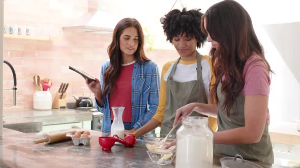 Women friends baking together in kitchen, using tablet for recipe ...