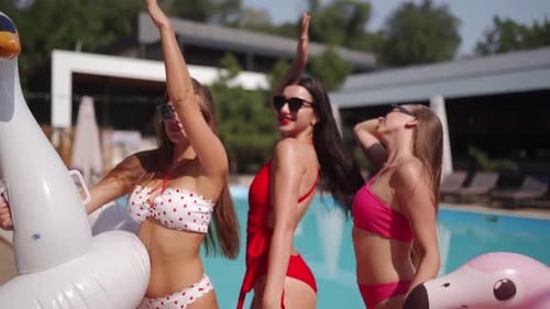 Women Models in Bright Colorful Bikinis and Sunglasses Posing at Swimming Pool Turquoise Water with