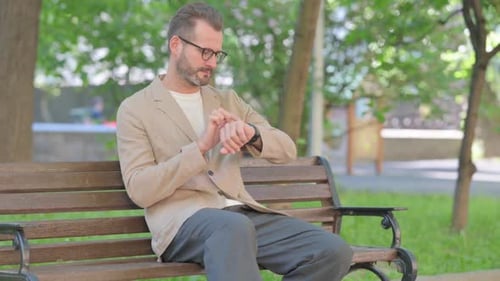 Man Checks Watch While Sitting on Park Bench
