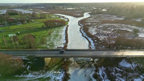Car Driving Through The Bridge Over Frozen River In Winter. - aerial shot