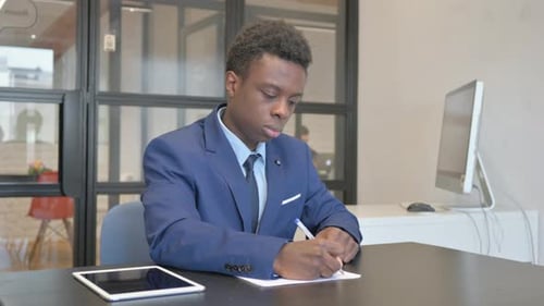 Junger afrikanischer Geschäftsmann schreibt am Arbeitsplatz einen Brief
