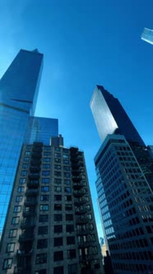 Des gratte-ciel en verre reflétant les bâtiments de la ville sous un soleil éclatant et un ciel bleu.