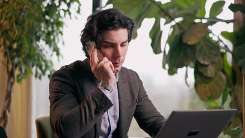 a serious man a businessman works at a laptop in the office communicates with colleagues smartphone