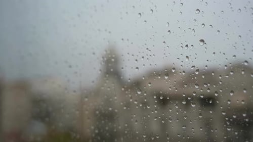 A slow-motion of raindrops seen through a window during heavy rainfall, with an urban city landscape