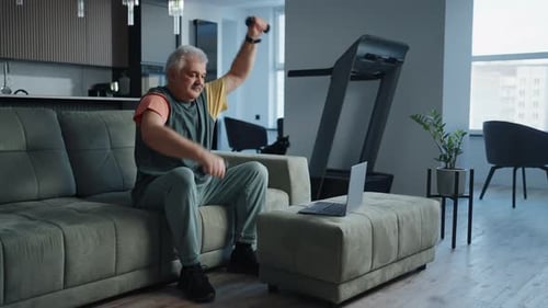 Active Elderly Man Doing Exercise With Dumbbells Sitting On Couch At Home Online Workout