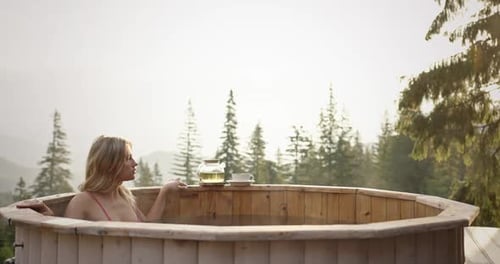 Woman Enjoying Hot Bath in Wooden Tub with Scenic Mountain Sunrise Drinking Tea