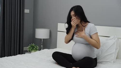 pregnant woman feeling nauseous on a bed
