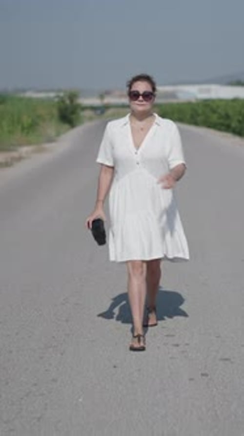 Young Curly Haired Blonde Caucasian Woman in a Short White Dress Walking Facing the Camera on a