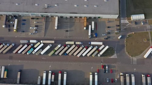 Semi truck with cargo trailer is travelling along a parking lot of a warehouse in the logistics park