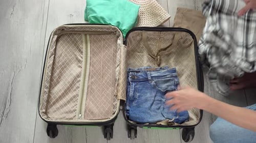 Guy opens the green baggage case and puts clothes in hand luggage. Tourist packing things