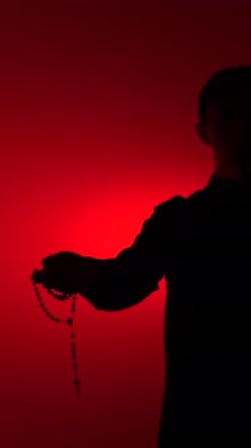 Silhouette of person holding rosary with red light