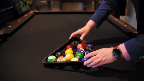Billardspieler verwendet ein hölzernes Regaldreieck und stellt zur Eröffnung des neuen Spiels Billardkugeln auf dem Tisch auf