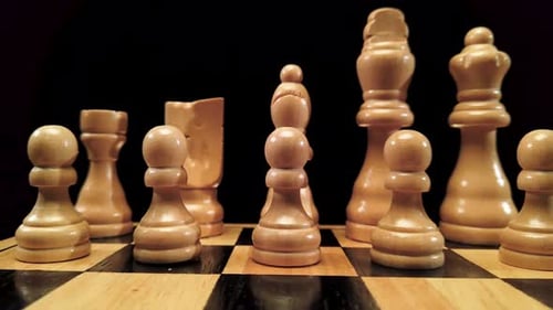 Truck shot from left to right of white chess pieces standing on a chessboard on a black background.