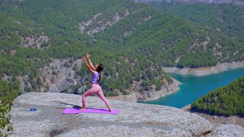 Woman Practicing Yoga on Rock Cliff with Panoramic Mountain and Lake View