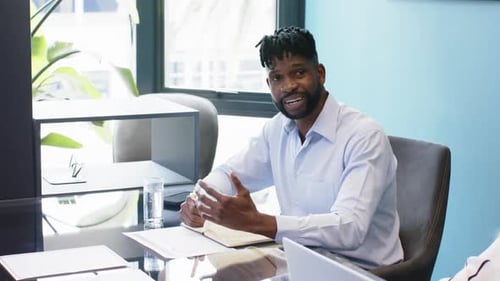 Smiling businessman sitting at desk in office meeting, holding pen and paper