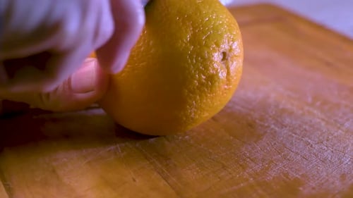 Cutting an orange in half on a wooden board. Close up.