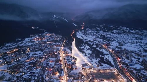 Nighttime View of a Snowy Valley with Twinkling Lights in the Alpine Town During Winter Season