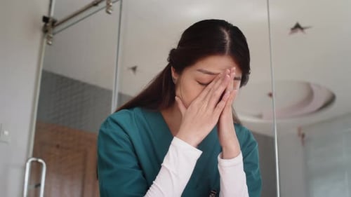 Worried Woman in Scrubs Puts Face in Hands