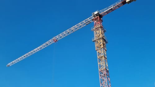 Tall Construction Tower Crane Rotating Its Jib Arm Against a Clear Blue Sky Heavy Lifting Machinery
