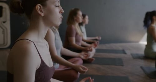 Tiltdown of Beautiful Young Ladies in Sportswear Meditating in Yoga Studio Together