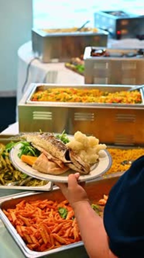 Person holding plate with grilled fish and potatoes at buffet.